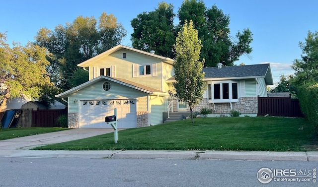 tri-level home featuring stone siding, driveway, a front lawn, and fence