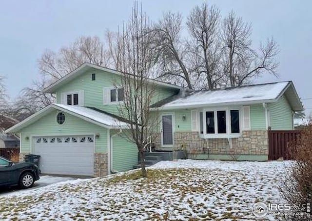 tri-level home with a garage, fence, stone siding, and driveway