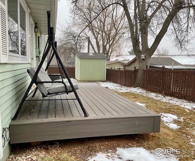 snow covered deck featuring an outbuilding, a fenced backyard, and a shed