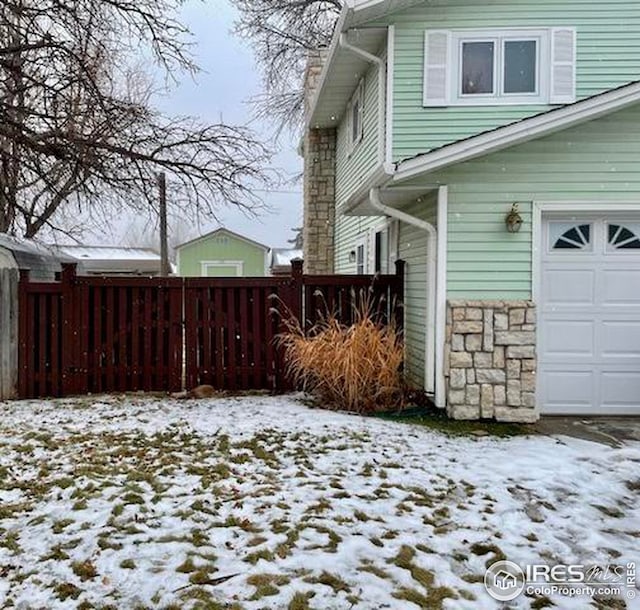 view of snow covered exterior featuring a garage, fence, stone siding, and a chimney