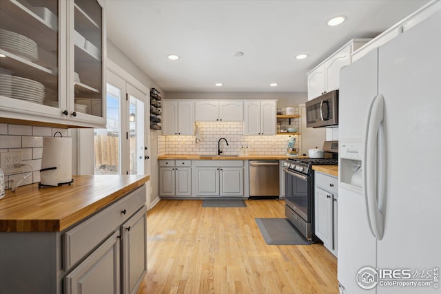 kitchen with light wood finished floors, white cabinets, butcher block countertops, glass insert cabinets, and stainless steel appliances