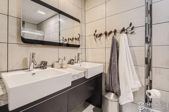 bathroom with a sink, tile walls, and double vanity