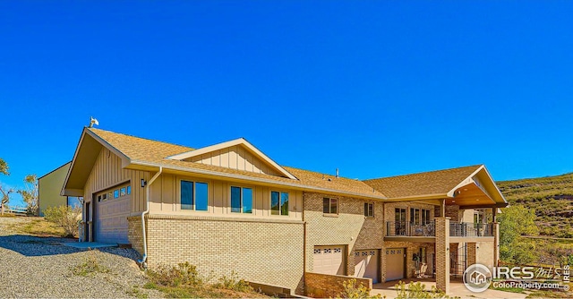 view of front of property with board and batten siding, brick siding, a balcony, and an attached garage