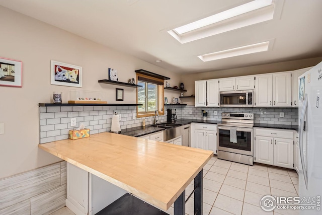 kitchen with stainless steel appliances, a peninsula, a sink, white cabinets, and open shelves