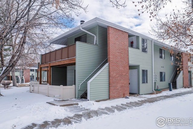 snow covered back of property featuring stairway