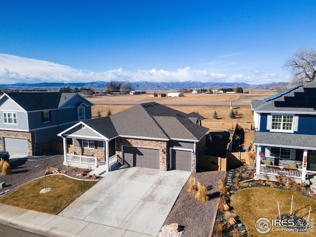 traditional-style home with driveway, stone siding, an attached garage, a mountain view, and a porch