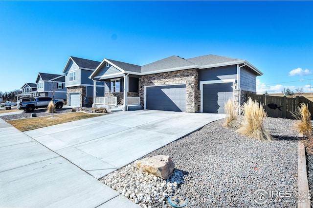 view of front of home with a porch, concrete driveway, fence, a garage, and stone siding