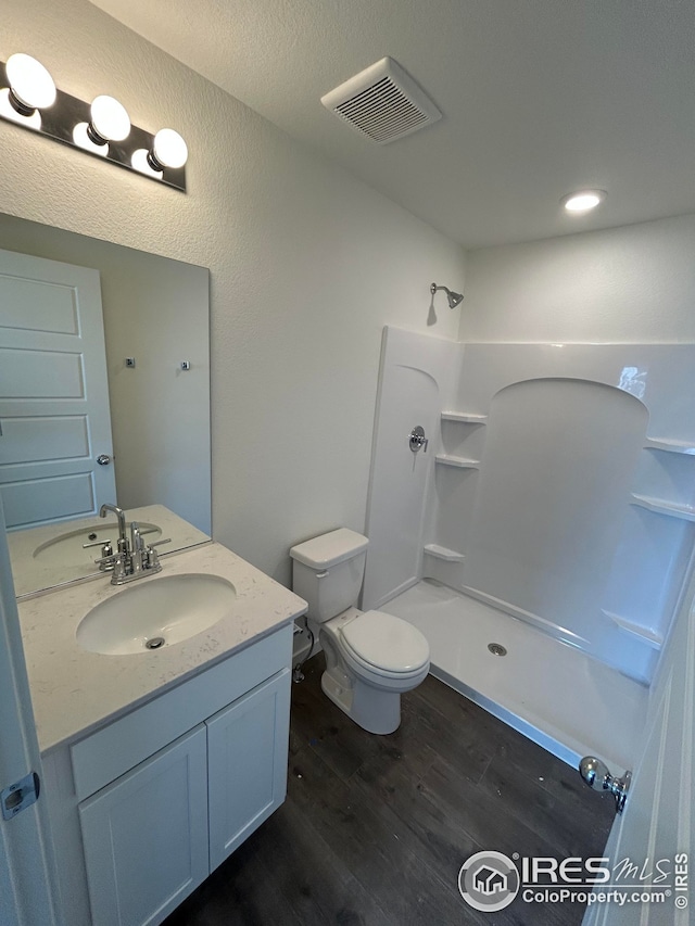 bathroom featuring visible vents, toilet, wood finished floors, walk in shower, and vanity