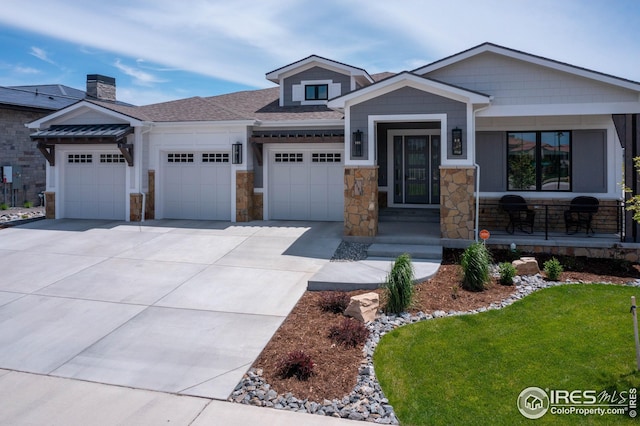 view of front facade featuring driveway, stone siding, a porch, a front yard, and a garage