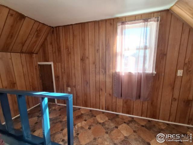 bonus room featuring vaulted ceiling and wood walls