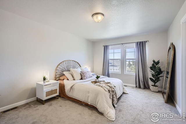 bedroom featuring light carpet, a textured ceiling, visible vents, and baseboards