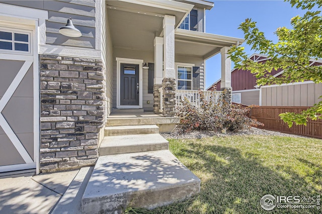 view of exterior entry with a yard, stone siding, covered porch, and fence