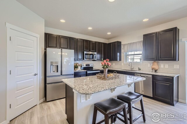 kitchen with decorative backsplash, a kitchen island, appliances with stainless steel finishes, a kitchen bar, and a sink