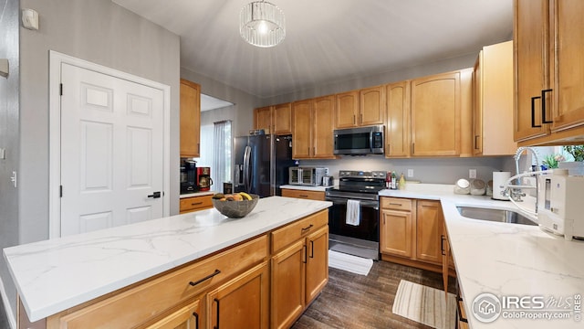 kitchen featuring appliances with stainless steel finishes, dark wood-type flooring, a kitchen island, a sink, and light stone countertops