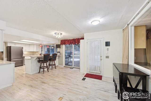 kitchen featuring light wood-style flooring, a peninsula, a breakfast bar, white cabinetry, and freestanding refrigerator