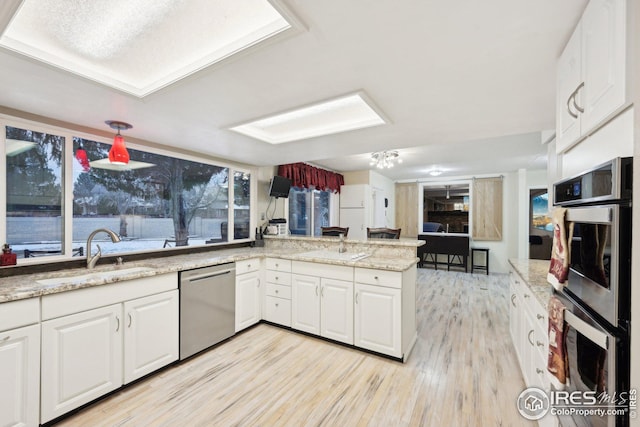 kitchen featuring light wood-style flooring, appliances with stainless steel finishes, white cabinetry, a sink, and a peninsula