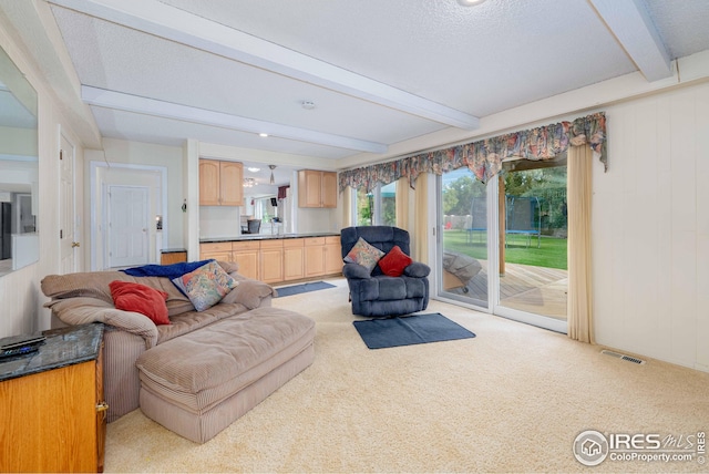 living room with light carpet, a textured ceiling, visible vents, and beamed ceiling