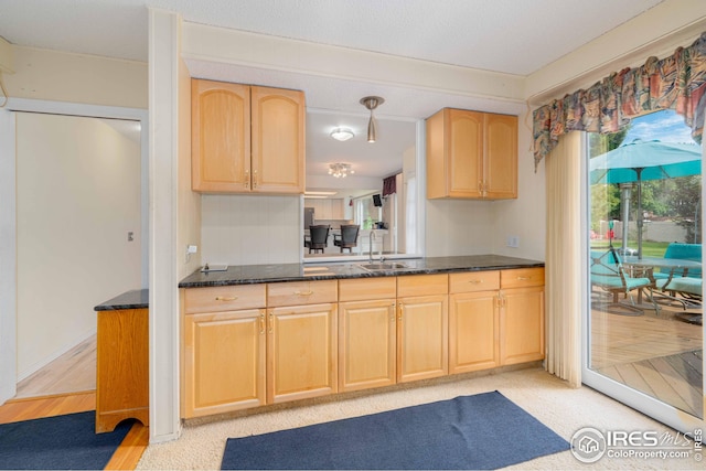 kitchen featuring dark stone counters, a sink, and light brown cabinetry