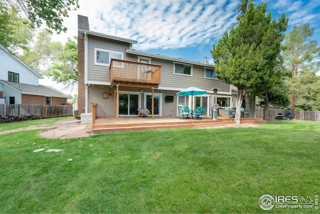 back of house featuring a chimney, a lawn, fence, a deck, and a balcony