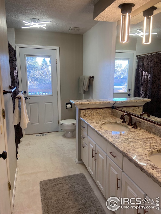 bathroom with double vanity, visible vents, toilet, a textured ceiling, and a sink