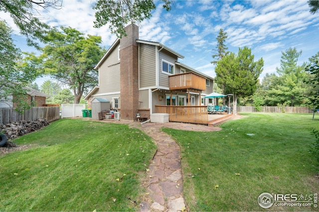 rear view of house featuring a fenced backyard, a chimney, a storage unit, and a yard