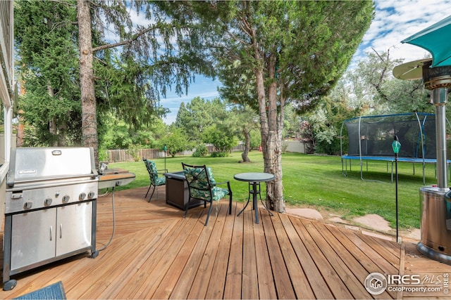 wooden terrace with a trampoline, a fenced backyard, a yard, and grilling area