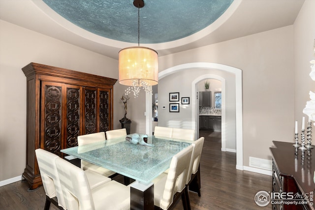 dining room with dark wood-style floors, arched walkways, a raised ceiling, and baseboards