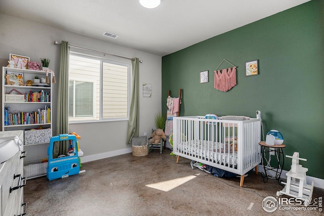 bedroom featuring concrete flooring, visible vents, a crib, and baseboards