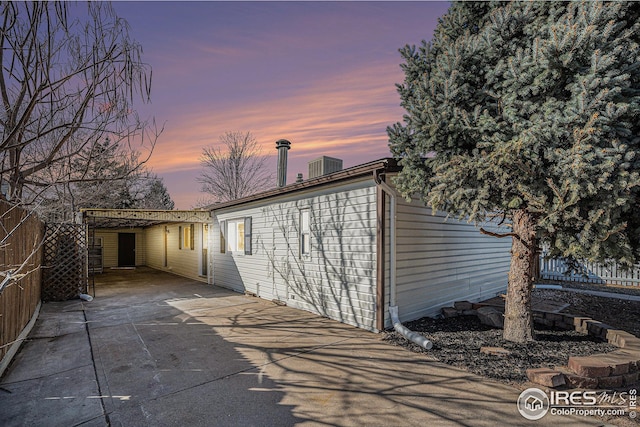 back of property at dusk featuring concrete driveway and fence