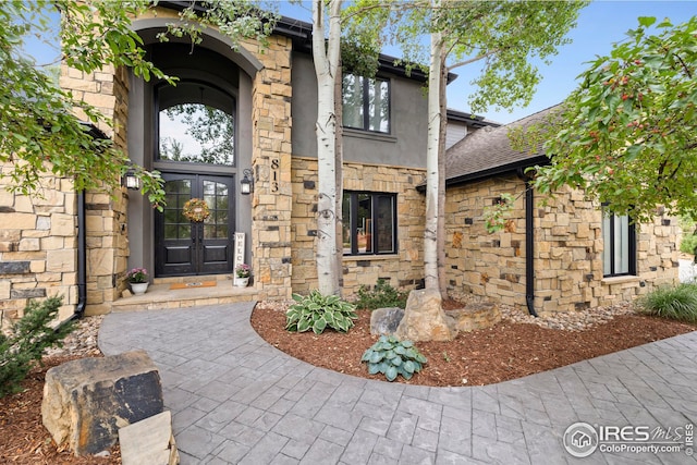 view of exterior entry with stone siding, french doors, and stucco siding