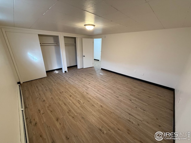 unfurnished bedroom featuring wood finished floors, two closets, and baseboards