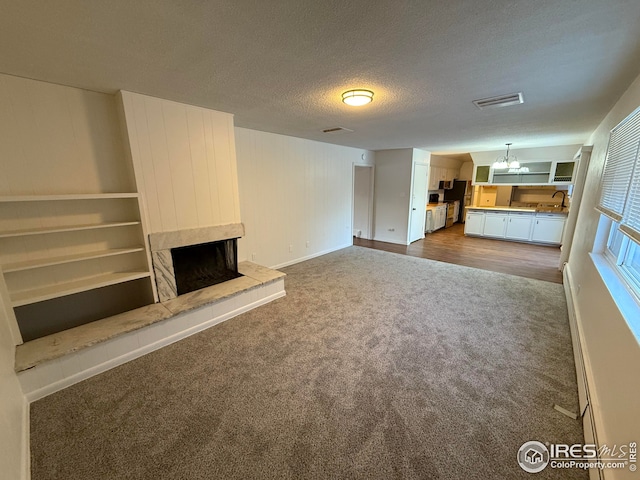 unfurnished living room featuring a textured ceiling, a baseboard heating unit, a sink, a high end fireplace, and dark carpet