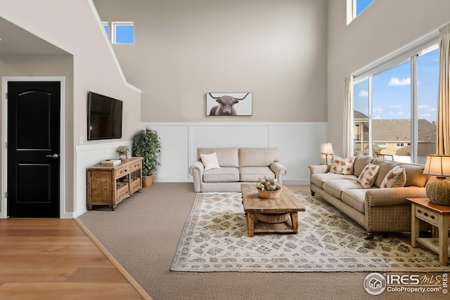 living area with a decorative wall, wainscoting, a high ceiling, and wood finished floors