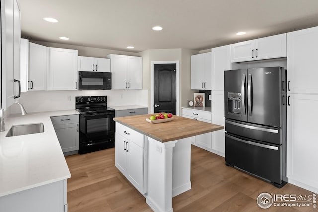 kitchen with butcher block counters, light wood-type flooring, a sink, and black appliances