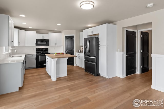 kitchen featuring a sink, a center island, black appliances, and light wood-style flooring