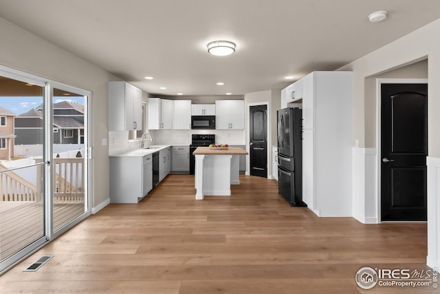 kitchen with light wood finished floors, visible vents, a sink, and black appliances