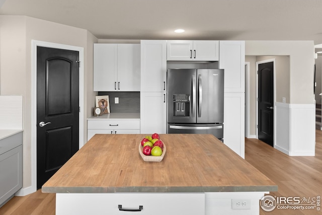 kitchen with light wood-style floors, stainless steel fridge with ice dispenser, white cabinets, a center island, and butcher block countertops