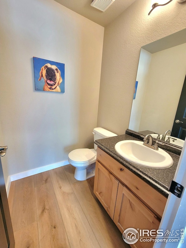 half bathroom with toilet, wood finished floors, vanity, and visible vents