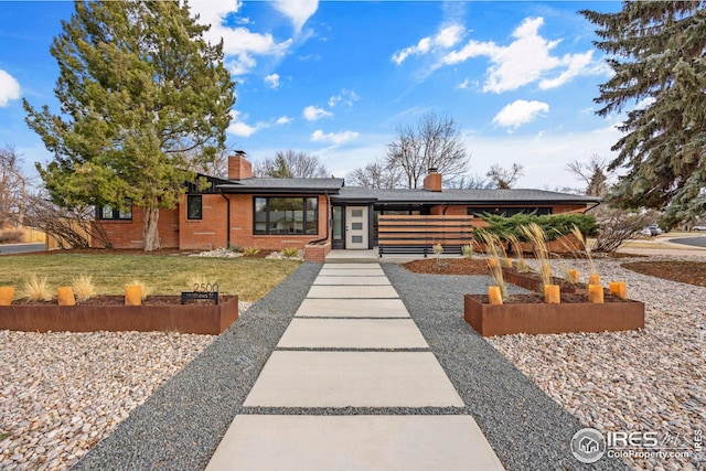 view of front of property featuring a front yard, brick siding, and a chimney