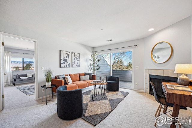 living room featuring a wealth of natural light, baseboards, carpet flooring, and a tiled fireplace