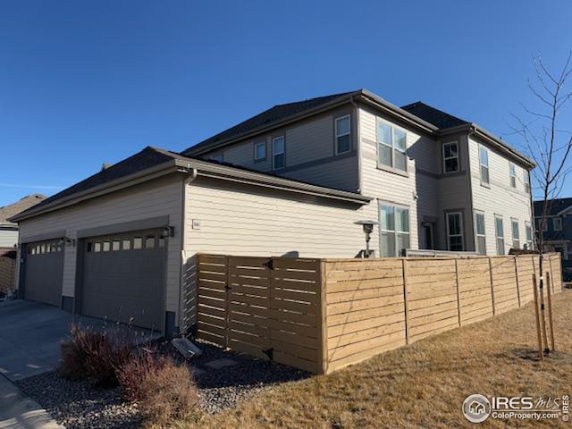 view of side of home with an attached garage, driveway, and fence