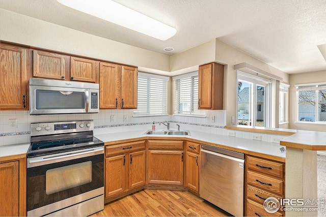 kitchen with a peninsula, stainless steel appliances, light countertops, a healthy amount of sunlight, and a sink