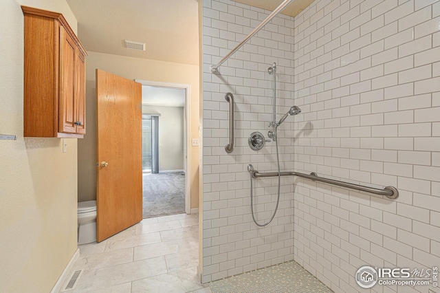 bathroom with toilet, baseboards, visible vents, and tiled shower