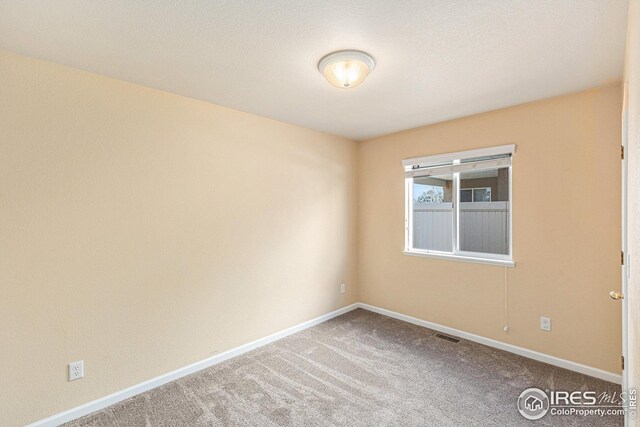 empty room featuring carpet floors, visible vents, and baseboards