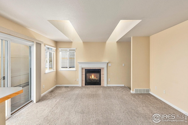 unfurnished living room with carpet, baseboards, visible vents, and a tiled fireplace