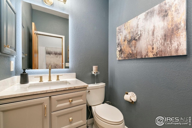 half bath with toilet, a textured wall, and vanity