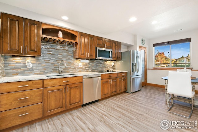 kitchen with decorative backsplash, light wood-style flooring, a sink, stainless steel appliances, and baseboards