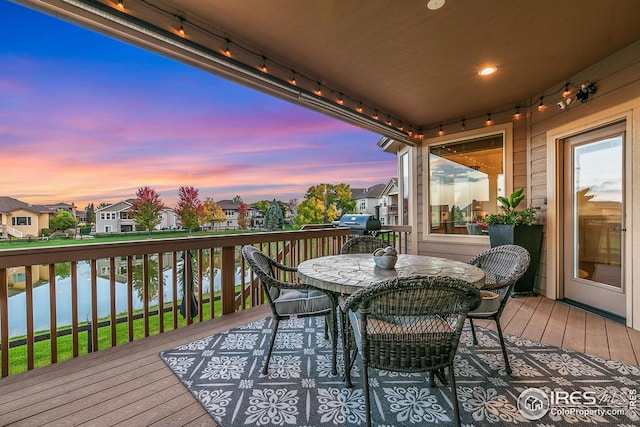 deck at dusk featuring a residential view, outdoor dining area, a water view, and a grill