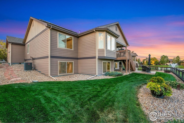 back of property at dusk with central AC, stairway, board and batten siding, and a yard