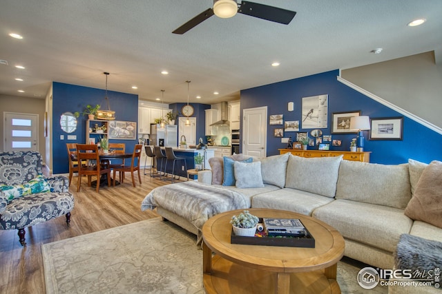 living room with a ceiling fan, light wood-type flooring, a textured ceiling, and recessed lighting